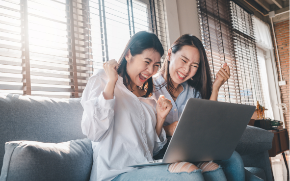 Two female students cheering as they look at a laptop screen