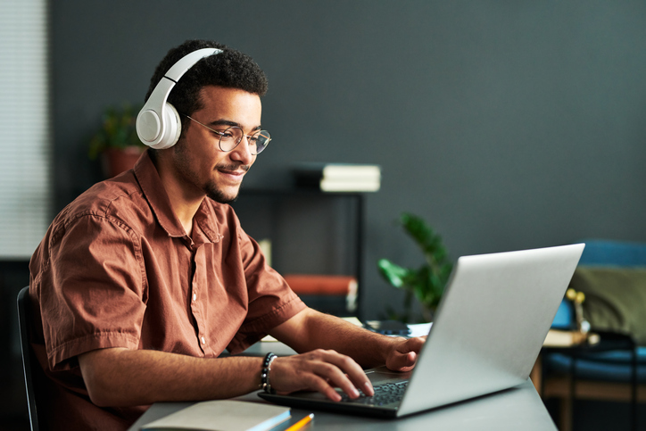 A young man in headphones smiling at his laptop